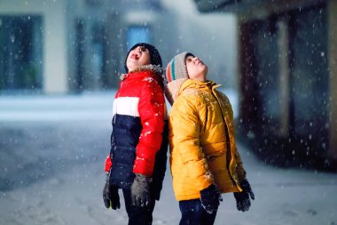 Sabahın erken saatlerinde okula yürüyen ilkokul öğrencisi iki küçük çocuk. Mutlu çocuklar eğleniyor ve ilk karla oynuyorlar. Kardeşler renkli kış kıyafetleri içinde arkadaşlar.