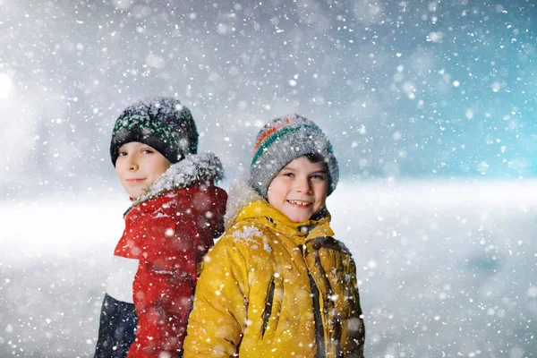 Sabahın erken saatlerinde okula yürüyen ilkokul öğrencisi iki küçük çocuk. Mutlu çocuklar eğleniyor ve ilk karla oynuyorlar. Kardeşler renkli kış kıyafetleri içinde arkadaşlar. — Stok fotoğraf