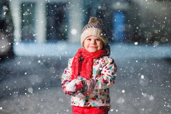 Urocza dziewczynka spacerująca zimą na świeżym powietrzu. Cute maluch podczas silnych opadów śniegu na wieczór. Dziecko bawiące się śniegiem. Noszenie ciepłe dziecko kolorowe ubrania i kapelusz z bąbelkami. — Zdjęcie stockowe