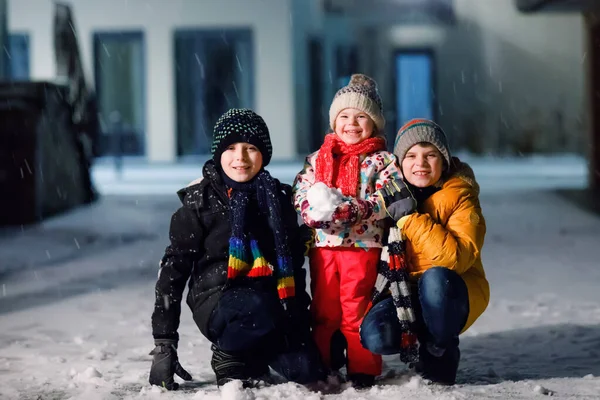 Dwóch małych chłopców i słodkie dziecko dziewczyna siedzi razem bawiąc się śniegiem w zimową noc. Rodzeństwo, bracia i siostrzyczka cieszą się silnymi opadami śniegu. Aktywna zabawa na rodzinne wakacje — Zdjęcie stockowe