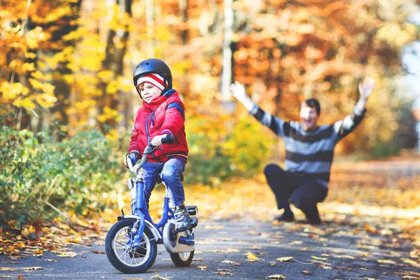 Kleine jongen die leert fietsen. Zijn vader leerde zijn zoon fietsen. Gelukkige man en kind. Actieve familie vrijetijdsbesteding. Kind met helm op de fiets. Veiligheid, sport, vrije tijd met kinderen concept. — Stockfoto