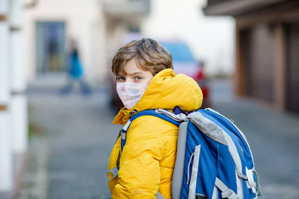 Маленький мальчик в медицинской маске по дороге в школу. Детский рюкзак. Школьник в зимний день с теплой одеждой. Время изоляции и карантина во время пандемии короны — стоковое фото