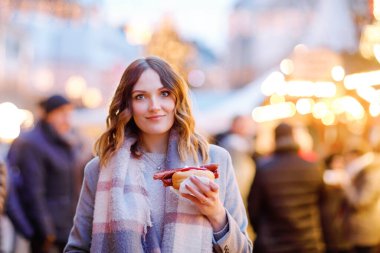 Güzel genç bir kadın, şiddetli kar yağışında geleneksel Noel pazarında eğleniyor. Sosis adı verilen geleneksel körili sosis yiyen mutlu kız. Aydınlatılmış Xmas ağacının yanında duran kadın.