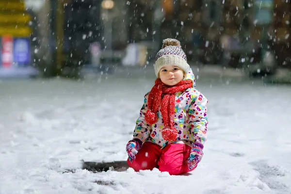 Urocza dziewczynka spacerująca zimą na świeżym powietrzu. Cute maluch podczas silnych opadów śniegu na wieczór. Dziecko bawiące się śniegiem. Noszenie ciepłe dziecko kolorowe ubrania i kapelusz z bąbelkami. — Zdjęcie stockowe