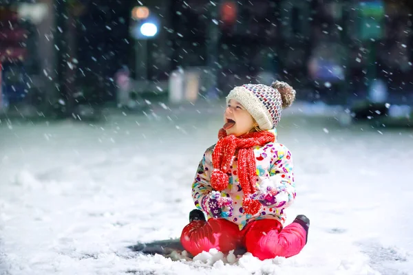 Urocza dziewczynka spacerująca zimą na świeżym powietrzu. Cute maluch podczas silnych opadów śniegu na wieczór. Dziecko bawiące się śniegiem. Noszenie ciepłe dziecko kolorowe ubrania i kapelusz z bąbelkami. — Zdjęcie stockowe