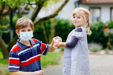 Liseli çocuk küçük kız kardeşine dezenfektanla el temizleme konusunda yardım ediyor. Kardeş ve tatlı küçük kız hijyen kurallarını öğreniyorlar. Coronavirus ve grip salgını sırasında aile. Covid virüs koruması.