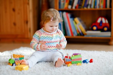 Küçük kız evde ya da çocuk odasında eğitici tahta oyuncaklarla oynuyor. Renkli trenle yürüyen çocuk. Çocuk farklı oyuncaklarla eğleniyor. Korona virüsü salgını sırasındaki yalnız çocuk karantina
