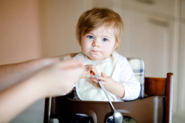 Adorable baby girl eating from spoon mashed vegetables and puree. food, child, feeding and people concept -cute toddler, daughter with spoon sitting in highchair and eating at home. — Stock Photo, Image