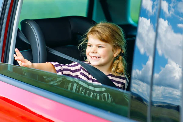 Adorable jeune fille assise dans un siège auto et regardant par la fenêtre sur la nature et la circulation. Petit enfant voyageant en voiture. Sécurité des enfants sur la route. Voyage en famille et vacances en été — Photo