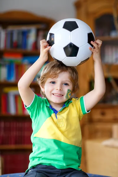 Piccolo bambino biondo in età prescolare con palla che guarda la partita di calcio in tv. Divertente felice pianto bambino fan divertirsi e tifare squadra di calcio vincente. — Foto Stock