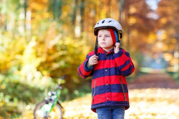 Criança ativa colocando capacete seguro antes de andar de bicicleta no dia ensolarado de outono na natureza. — Fotografia de Stock