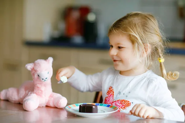 Linda niña divertida comiendo helado de chocolate en casa. Feliz bebé sano niño alimentación peluche lama juguete con helado dulce. Niño encantador disfrutando de postre pudín. —  Fotos de Stock