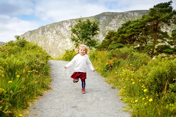 Roztomilé malé šťastné batole dívka běží na naučné stezce v Glenveagh národním parku v Irsku. Usmívající se a smějící se dítě baví trávení rodinných prázdnin v přírodě. Cestování s malými dětmi — Stock fotografie