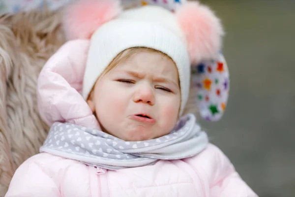 Sad crying hungry baby girl sitting in the pram or stroller on cold autumn, winter or spring day. Weeping child in warm clothes, fashion stylish baby coat and hat. Snow falling down — Stock Photo, Image