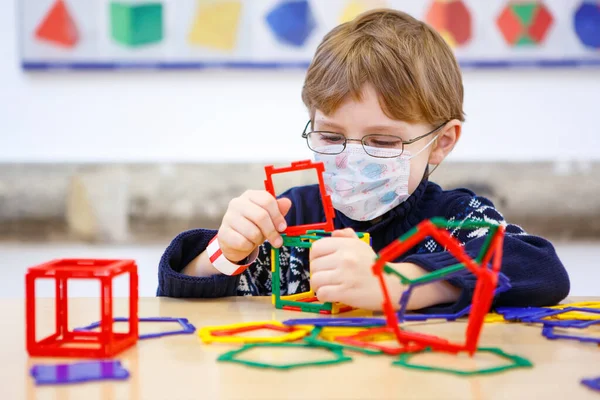 Criança com máscara médica brincando com lotes de blocos de plástico colorido kit no berçário pré-escolar ou escola primária. Equipamento de proteção de uso infantil bonito como luta contra o covid 19 corona vírus. — Fotografia de Stock