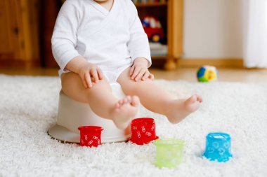 Lazımlığın üzerinde oturan küçük, tatlı, yaşlı, küçük kız bebek. Çocuk eğitim oyuncağı ve tuvalet eğitimi konseptiyle oynuyor. Bebek öğrenme, gelişme adımları. Yüzü yok, tanınmayan biri..