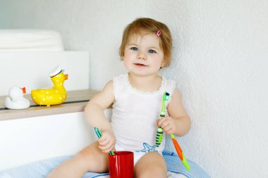 Küçük kız diş fırçası tutuyor ve ilk dişlerini fırçalıyor. Bebek süt dişini temizlemeyi öğreniyor..