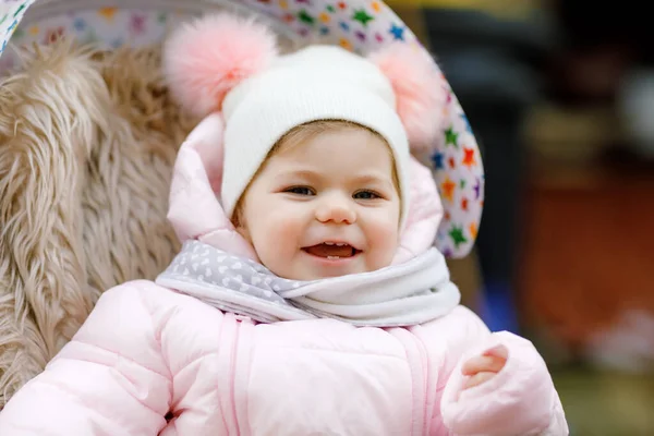 可爱的小女孩在寒冷的秋天，冬天或春天坐在婴儿车或婴儿车里。快乐的孩子，穿着温暖的衣服，时髦的婴儿外套和帽子。雪花飘落 — 图库照片