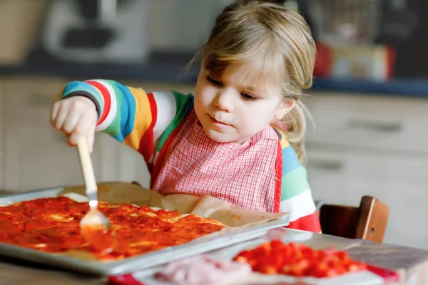 Очаровательная маленькая девочка, готовит итальянскую пиццу дома. Милый счастливый ребенок веселится на домашней кухне, в помещении. Ребенок, дошкольник, помогающий и готовящий здоровое питание — стоковое фото