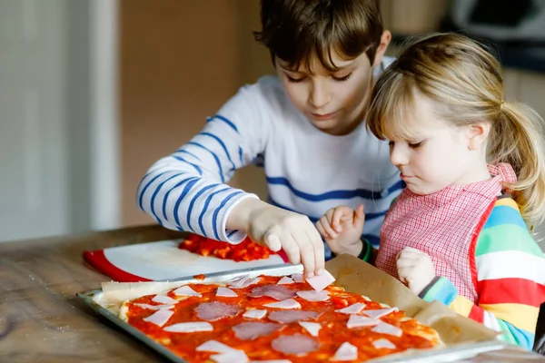 İki kardeş, evde İtalyan pizzası yapan küçük çocuklar. Şirin kız ve okul çocuğu ev mutfağında, evde eğleniyorlar. Erkek ve kız kardeş, aile yemeği hazırlıyor.