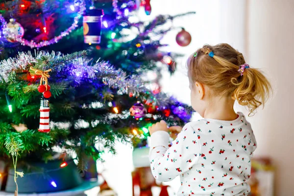 Adorable jeune fille en pyjama décorant arbre de Noël avec jouet dans de jolies mains. Petit enfant en tenue de nuit debout près de l'arbre de Noël. célébration des vacances d'hiver traditionnelles en famille — Photo