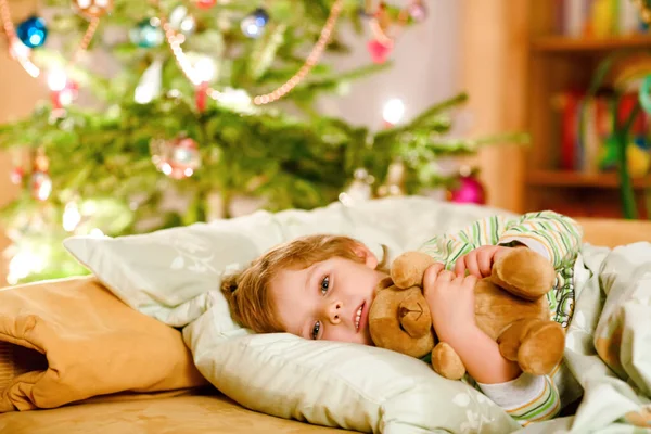 Little cute blond boy sleeping under Christmas tree and dreaming of Santa at home, indoors. Traditional Christian festival. Happy kid child waiting for gifts on xmas. Cozy soft light — Stock Photo, Image