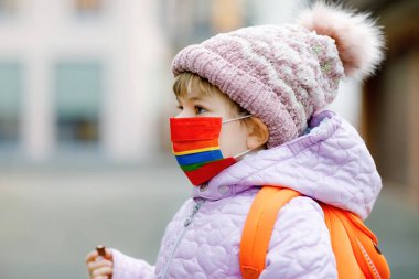 Anaokuluna, çocuk parkına ya da kreşe giderken maske takan küçük bir çocuk. Soğuk bir günde sırt çantalı bir çocuk ve sıcak giysiler. Corona salgını sırasında tecrit ve karantina süresi