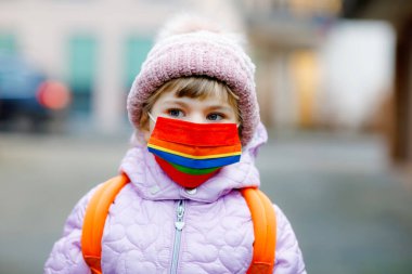 Anaokuluna, çocuk parkına ya da kreşe giderken maske takan küçük bir çocuk. Soğuk bir günde sırt çantalı bir çocuk ve sıcak giysiler. Corona salgını sırasında tecrit ve karantina süresi