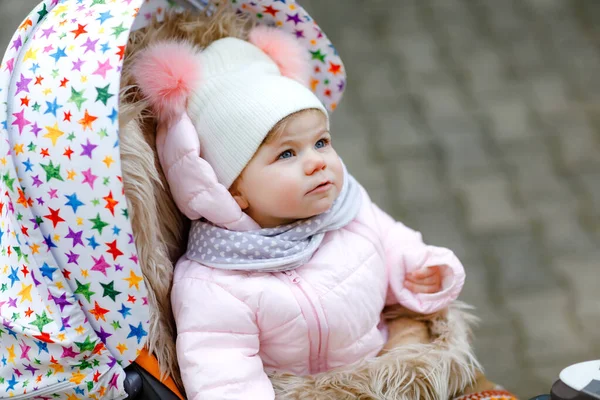 Linda niña hermosa sentada en el cochecito o cochecito en el frío otoño, invierno o día de primavera. Feliz niño sonriente en ropa de abrigo, abrigo de bebé con estilo de moda y sombrero. Nieve cayendo — Foto de Stock