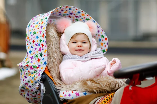 可爱的小女孩在寒冷的秋天，冬天或春天坐在婴儿车或婴儿车里。快乐的孩子，穿着温暖的衣服，时髦的婴儿外套和帽子。雪花飘落 — 图库照片
