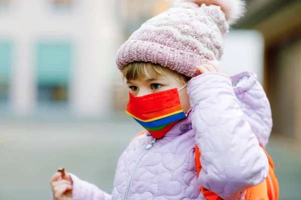 Little kid girl wearing medical mask on the way to kindergarten, playschool or nursery. Child with backpack satchel on cold day with warm clothes. Lockdown and quarantine time during corona pandemic — Stock Photo, Image