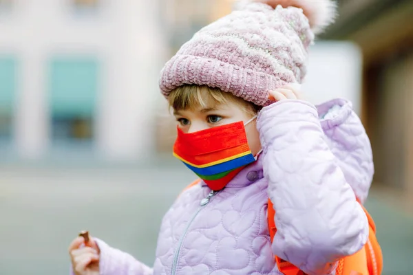 Menina criança vestindo máscara médica no caminho para o jardim de infância, playschool ou berçário. Criança com mochila mochila no dia frio com roupas quentes. Fechamento e tempo de quarentena durante a pandemia de corona — Fotografia de Stock