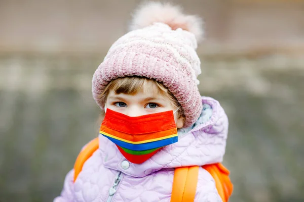 Little kid girl wearing medical mask on the way to kindergarten, playschool or nursery. Child with backpack satchel on cold day with warm clothes. Lockdown and quarantine time during corona pandemic — Stock Photo, Image