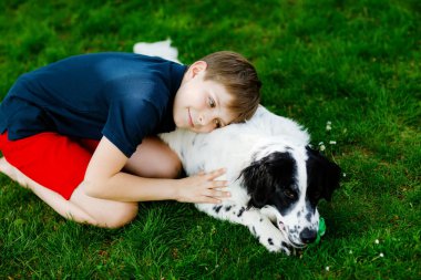 Aktif çocuk bahçede aile köpeğiyle oynuyor. Gülen okul çocuğu köpekle eğleniyor, koşuyor ve topla oynuyor. Dışarıda mutlu bir aile. Hayvanlar ve çocuklar arasındaki dostluk ve sevgi