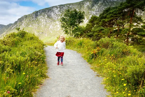 Linda niñita feliz corriendo por el sendero de la naturaleza en el parque nacional Glenveagh en Irlanda. Niño sonriente y riente que se divierte pasando vacaciones familiares en la naturaleza. Viajar con niños pequeños — Foto de Stock