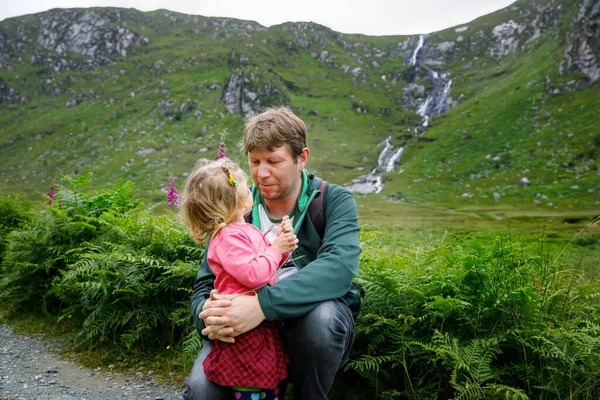 Pequeña niña feliz abrazándose con su padre en el parque nacional Glenveagh en Irlanda. Sonriendo y riendo bebé niño y hombre divirtiéndose pasando vacaciones familiares en la naturaleza. Viajar con niños pequeños — Foto de Stock