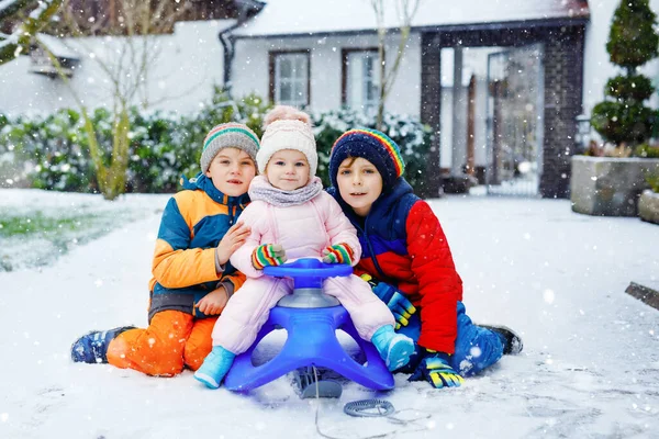 Dwóch małych chłopców i urocza dziewczynka siedząca razem na saniach. Rodzeństwo, bracia i siostrzyczka cieszą się jazdą saniami podczas opadów śniegu. Dzieci jeżdżące na śniegu. Aktywna zabawa na rodzinne wakacje — Zdjęcie stockowe