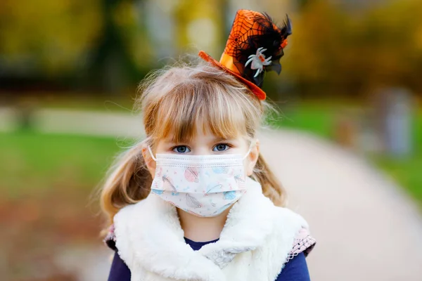 Little toddler girl dressed as a witch with medical mask on face. Child outdoors, during Pandemic corona virus quarantine lockdown time wearing protective equipment — Stock Photo, Image
