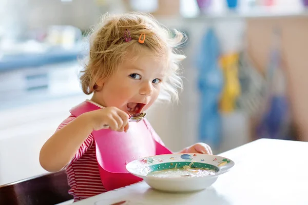 Adorable baby girl eating from spoon vegetable noodle soup. food, child, feeding and development concept. Cute toddler child, daughter with spoon sitting in highchair and learning to eat by itself Stock Image