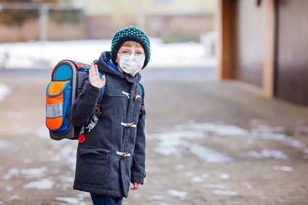 Маленький хлопчик в окулярах носить медичну маску на шляху до школи після замикання. Дитячий рюкзак. Школярка в зимовий день з теплим одягом. Карантинний час під час пандемії корона — стокове фото