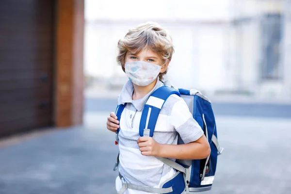 Маленький хлопчик в окулярах носить медичну маску на шляху до школи після замикання. Дитячий рюкзак. Школярка в теплий день зі шкільною формою. Карантинний час під час пандемії корона — стокове фото