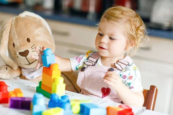 Imádnivaló kisbaba lány kedvenc plüss nyuszi játszik oktatási játékok óvodában. Boldog egészséges gyermek szórakozás színes különböző műanyag blokkok otthon. Aranyos baba tanulás létrehozása. — Stock Fotó