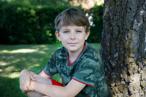 Retrato al aire libre del niño preadolescente feliz sonriente en el soleado día de verano en el parque cerca del árbol. Hermoso niño sano en ropa colorida actividad al aire libre — Foto de Stock