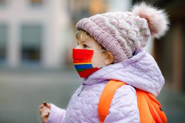 Anaokuluna, çocuk parkına ya da kreşe giderken maske takan küçük bir çocuk. Soğuk bir günde sırt çantalı bir çocuk ve sıcak giysiler. Corona salgını sırasında tecrit ve karantina süresi