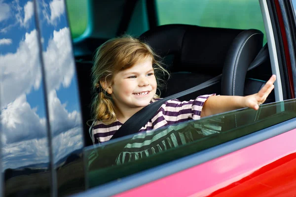 Adorable jeune fille assise dans un siège auto et regardant par la fenêtre sur la nature et la circulation. Petit enfant voyageant en voiture. Sécurité des enfants sur la route. Voyage en famille et vacances en été — Photo