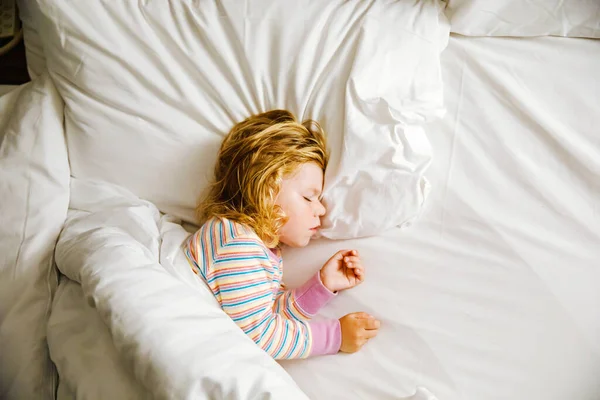 Linda niña pequeña durmiendo en la cama grande de los padres. Niño adorable soñando en la cama del hotel en vacaciones familiares o en casa. — Foto de Stock