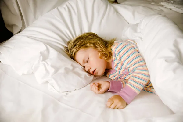 Χαριτωμένο κοριτσάκι που κοιμάται στο μεγάλο κρεβάτι των γονιών. Αξιολάτρευτο παιδί που ονειρεύεται στο κρεβάτι του ξενοδοχείου για οικογενειακές διακοπές ή στο σπίτι. — Φωτογραφία Αρχείου