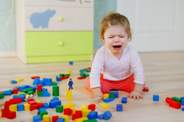 Eğitici oyuncaklarla ağlayan bir kız çocuğu. Üzgün, aç, yalnız, sağlıklı çocuk evde ya da çocuk odasında renkli tahta blokların yanında oturuyor. Bebek kreşte kayıp anne.
