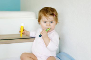 Küçük kız diş fırçası tutuyor ve ilk dişlerini fırçalıyor. Bebek süt dişini temizlemeyi öğreniyor. Önleme, hijyen ve sağlık hizmetleri kavramı. Banyoda mutlu bir çocuk