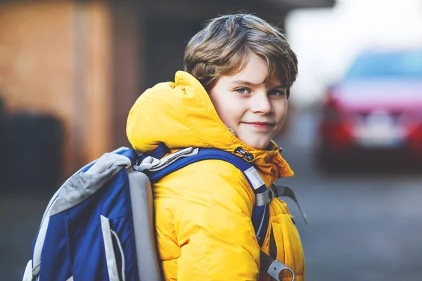 Chłopiec z podstawówki, idący do szkoły. Portret szczęśliwego dziecka na ulicy z korkami. Student w żółtej kurtce i plecaku w kolorowe ubrania zimowe. — Zdjęcie stockowe